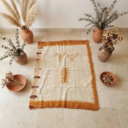 Bohemian style beige and orange rug with geometric patterns surrounded by dried floral arrangements in terracotta vases