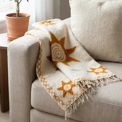Plaid beige motif soleil orange à franges posé sur canapé tissu beige clair et coussin