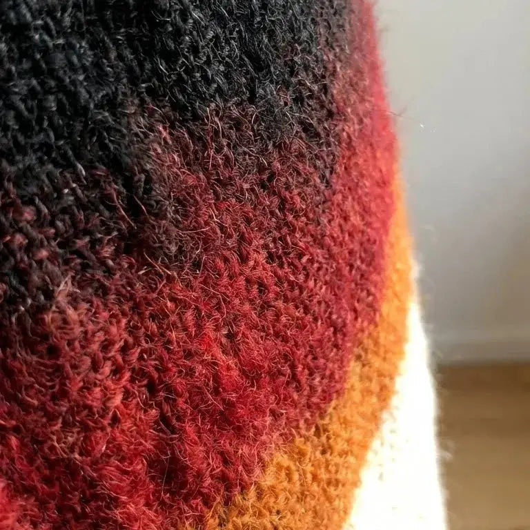 Détail de tissu tricoté en laine avec dégradé de couleurs noir, rouge, orange et blanc