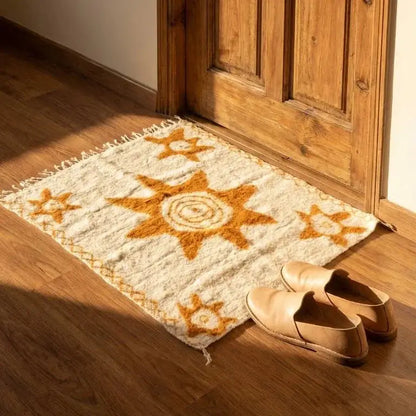 Tapis beige avec motif soleil orange devant porte en bois, chaussures en cuir beige au sol