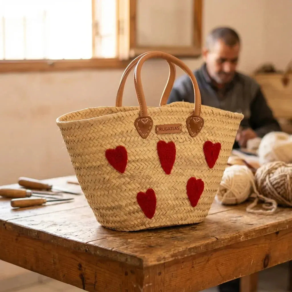Handwoven straw bag with leather handles and red heart decorations on wooden table in artisan workshop