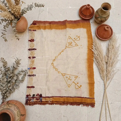 Handwoven Berber rug with geometric patterns on stone floor, surrounded by terracotta pots and dried plants