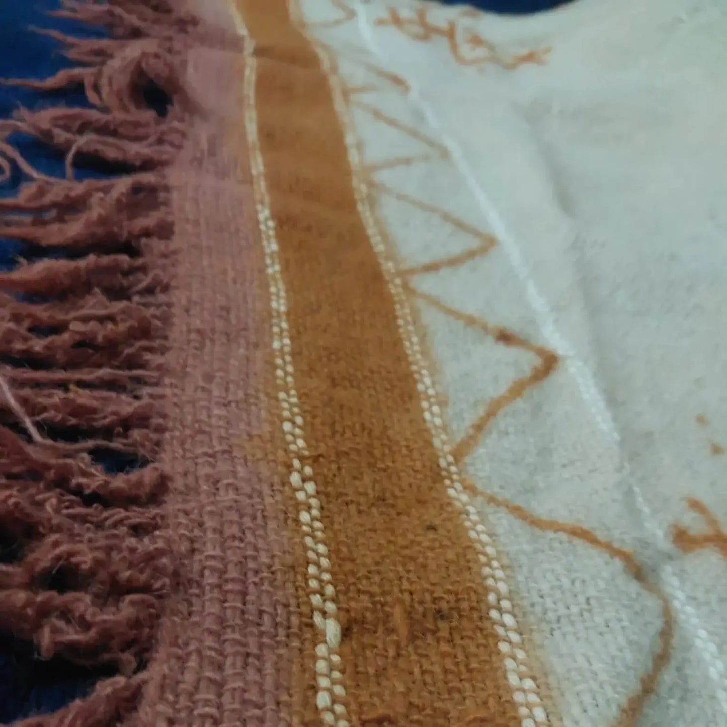Close-up of woven fabric with rust, cream, and orange geometric patterns and fringed edge