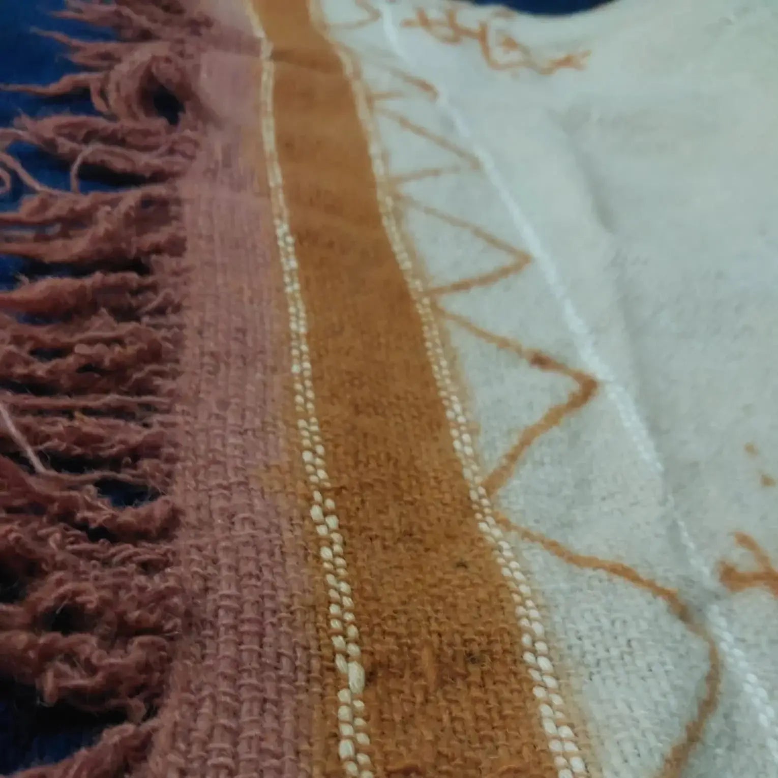 Close-up of woven fabric with rust, cream, and orange geometric patterns and fringed edge