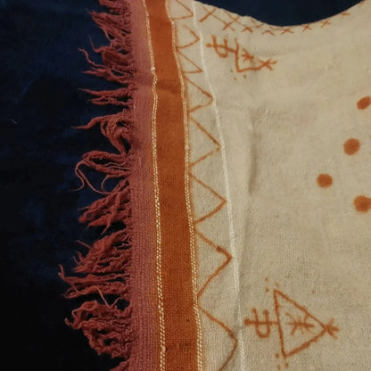 Close-up of beige fabric with orange tribal patterns and fringe on dark background