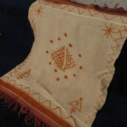 Beige woven textile with rust orange geometric and star patterns, and fringed edges on dark fabric
