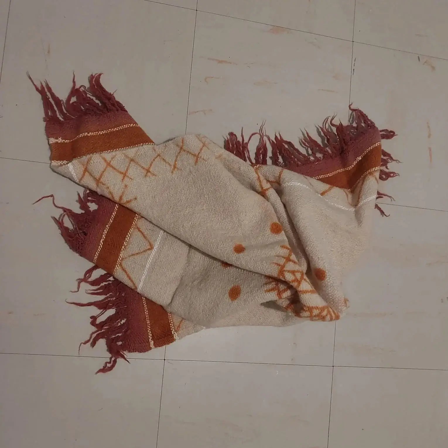 Beige and rust woven blanket with fringes and geometric patterns on tiled floor