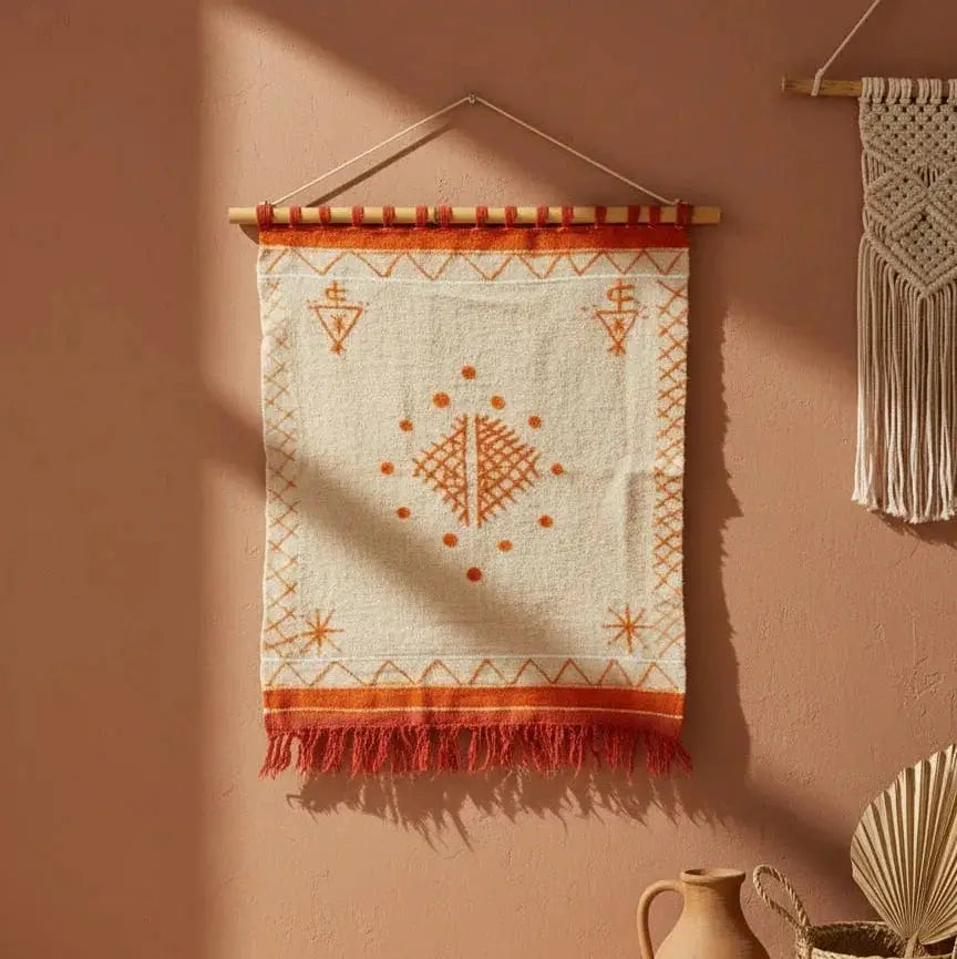 Boho wall hanging with orange geometric patterns and fringe, on warm terracotta wall