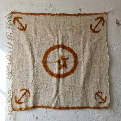 Tapis beige avec motifs orange étoile centrale et quatre flèches aux coins, suspendu sur mur texturé