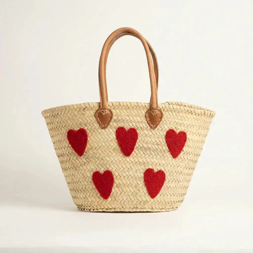 Woven straw tote bag with tan leather handles and five red heart-shaped patches on front