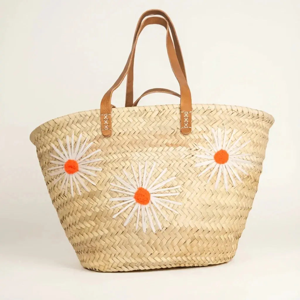 Woven straw tote bag with leather handles and three white and orange flower appliques