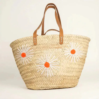 Woven straw tote bag with leather handles and three white and orange flower appliques